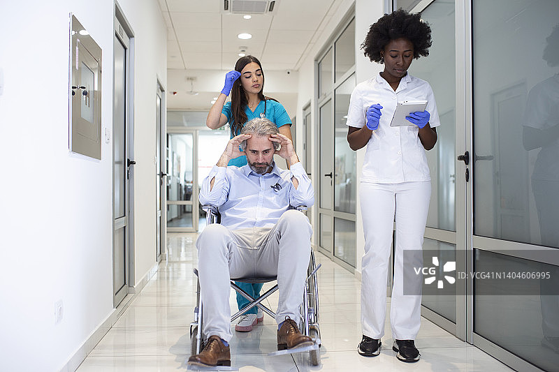 轮椅病人与专业的非裔美国女医生和护士专科人员在医院康复中心走廊图片素材