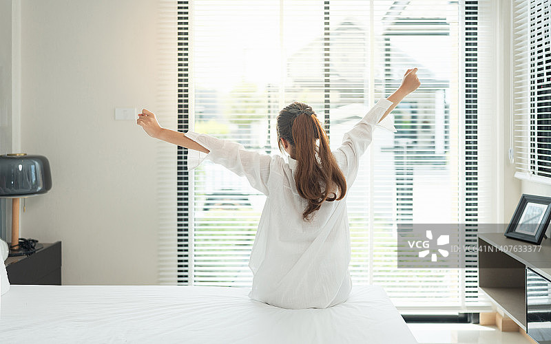 亚洲女性起床伸展放松在家里的卧室。清晨早出，醒来休息晴天。生活方式的概念图片素材