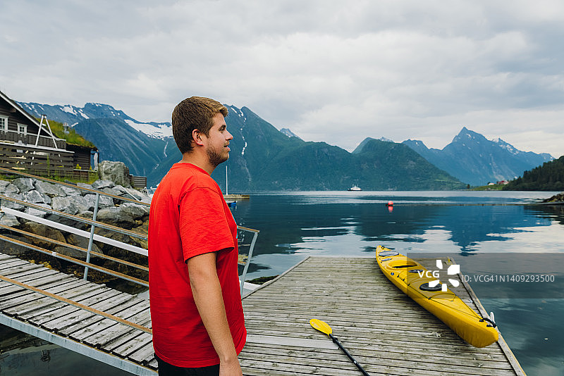 一名男子旅行者准备在挪威风景优美的峡湾划皮划艇的侧面视图图片素材
