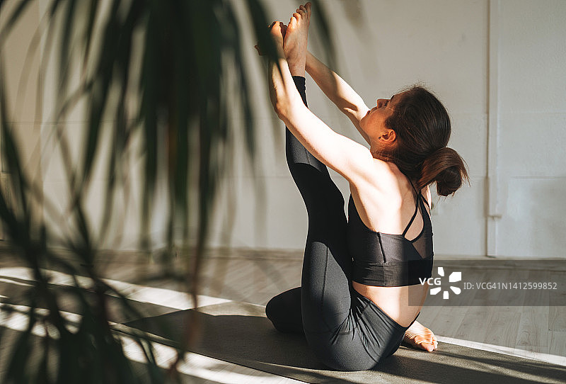 年轻的健身女性练习瑜伽做体式在轻瑜伽工作室与绿色的房子植物图片素材