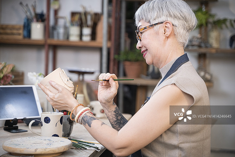 一名女性正在用画笔为陶瓷杯子作画。图片素材