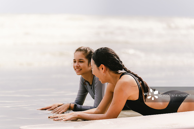 美丽的母亲和女儿玩冲浪板与微笑。海边度假阖家欢乐图片素材