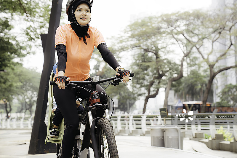 一名穆斯林妇女在公园骑自行车，她的孩子坐在副驾驶上图片素材