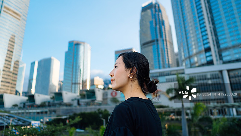 侧面的自信年轻的亚洲女商人展望积极的情绪，站在繁华的城市城市天际线在市中心区。女孩的力量。职场上成功的女性企业家。女性的领导能力和对成功的决心图片素材