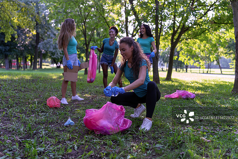 快乐的多种族年轻女性正在用塑料袋收集垃圾。图片素材