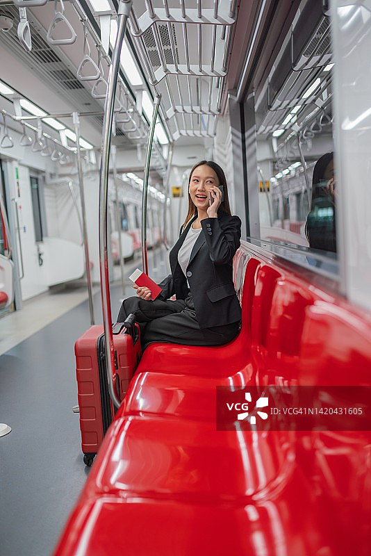一个年轻的亚洲女商人的肖像照片旅行在通勤火车与她的手机和红色行李去商务旅行图片素材