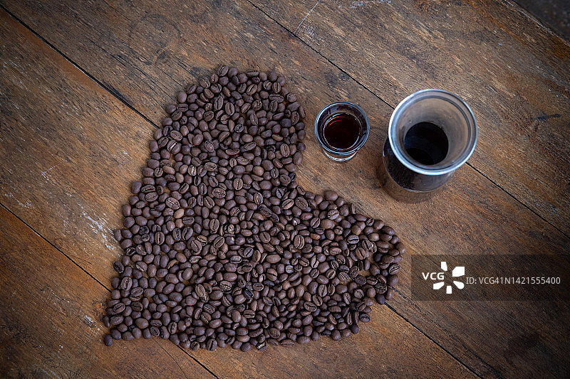 烤好的咖啡豆放在桌子上，呈心形，配上一杯咖啡图片素材