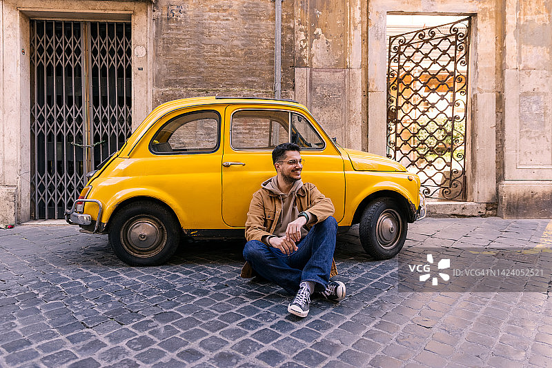 意大利罗马，一名快乐的微笑男子坐在一辆黄色小轿车旁图片素材
