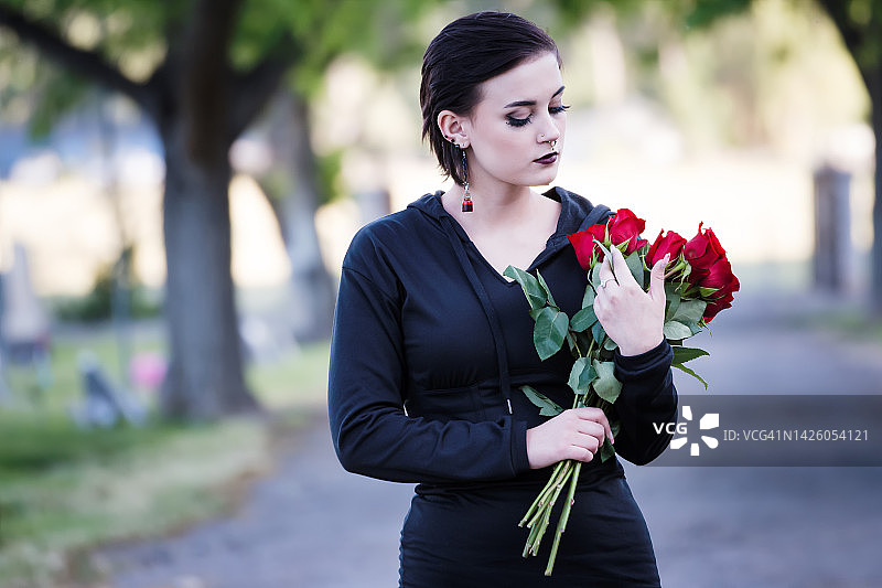 一个十几岁的女孩在墓地拿着花。图片素材