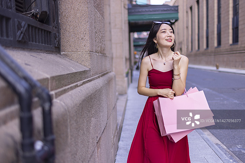 一名快乐的亚洲妇女拿着购物包走在上海外滩街上，概念照图片素材