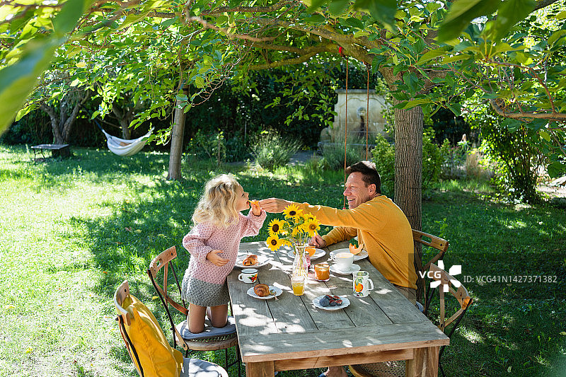 父亲在花园里吃早餐时给女儿喂瓜图片素材