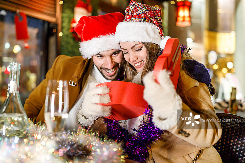 现代的年轻夫妇坐在咖啡馆里，享受圣诞礼盒。图片素材