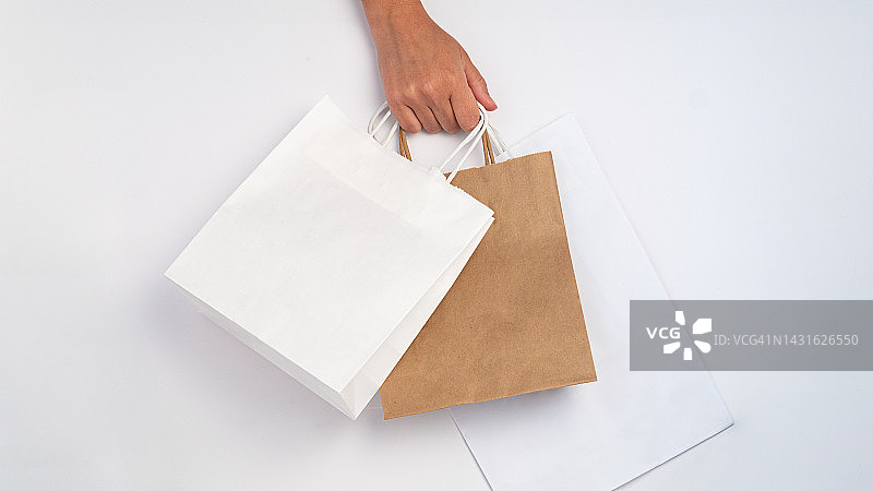 女人手拎购物袋，白色和牛皮纸款式，打折出售图片素材
