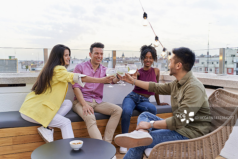 四个穿着讲究的不同种族的朋友坐在露台上，用白葡萄酒举杯共饮图片素材