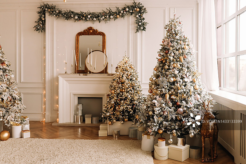 圣诞节的概念。在冬天的新年前夜，公寓宽敞明亮的客厅里有一个豪华的现代风格的壁炉，装饰着圣诞球和圣诞树花环。文本的地方图片素材