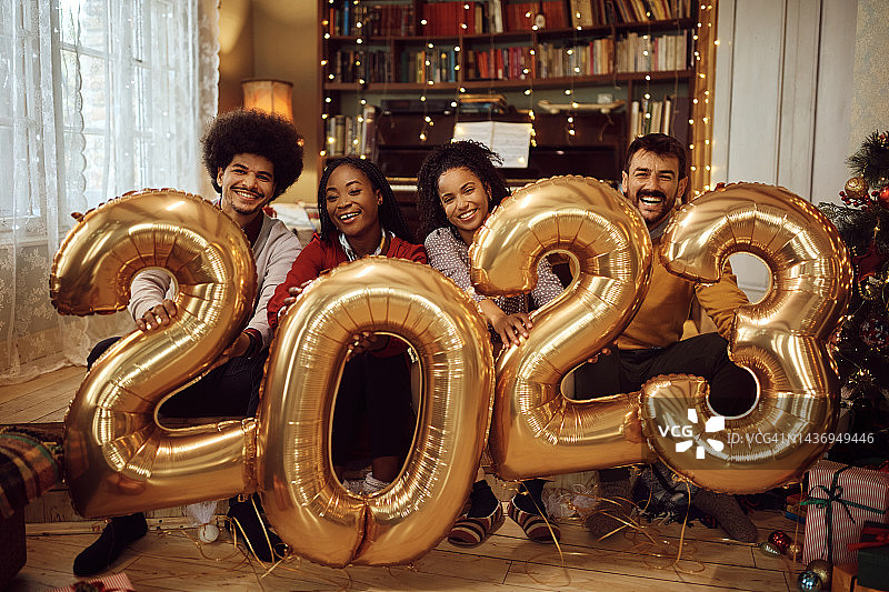 快乐的朋友们拿着气球，在家里看着相机庆祝2023年。图片素材