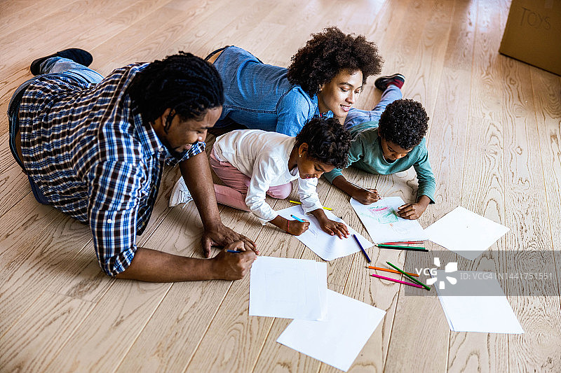 上图是幸福的黑色家庭在家里的地板上着色。图片素材