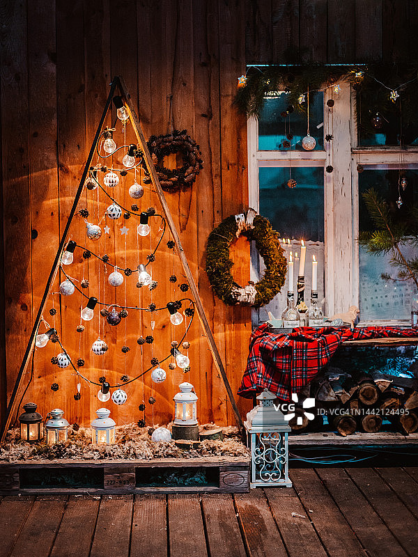带有美式圣诞装饰的乡村别墅的冬季外观。白雪覆盖的院子里有门廊、树、白色长凳和老式木制雪橇。图片素材