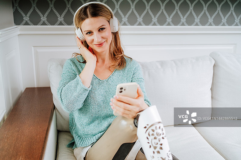 在家听播客。满意的女人用假腿在家里用手机听音乐图片素材