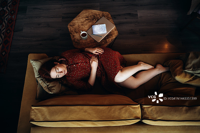 画像上有一个长头发的红头发的女人躺在沙发上，端着一杯茶图片素材