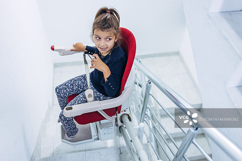 小女孩坐在残疾人专用的红色楼梯椅上图片素材