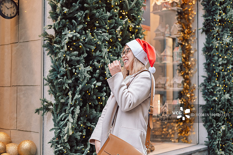快乐的女人戴着圣诞老人的帽子在街上微笑图片素材