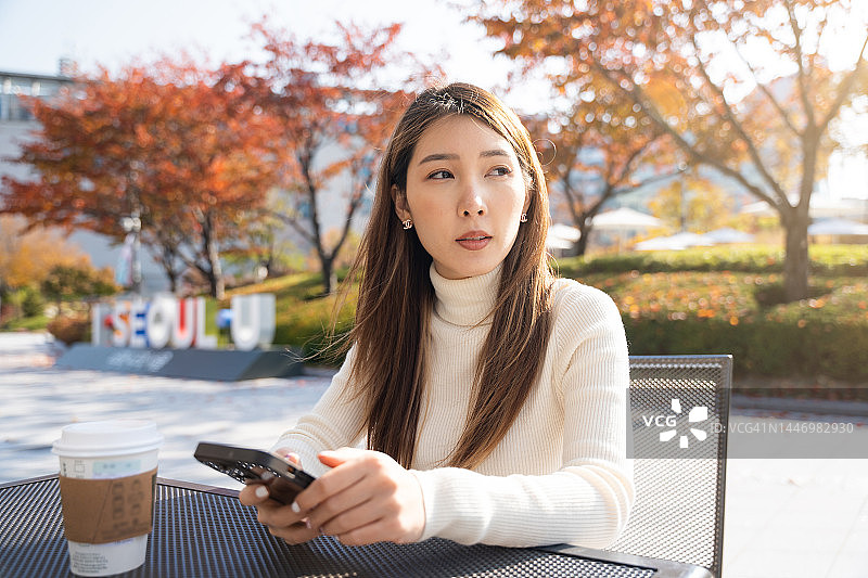 早晨，一名亚洲女子坐在首尔的公园里使用智能手机图片素材