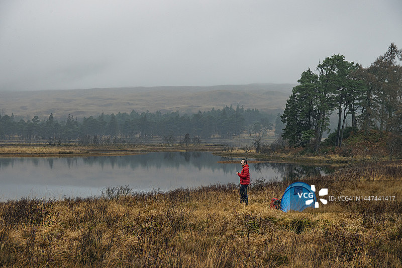 一位成熟的男子在苏格兰的一个湖边露营，欣赏着美丽的薄雾美景。图片素材