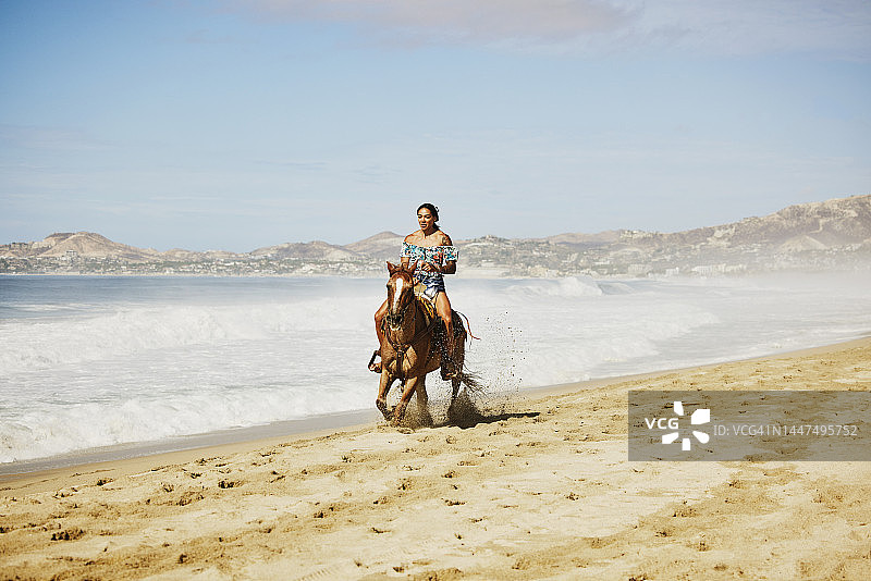 宽阔的镜头，微笑的女人在热带海滩上骑马驰骋图片素材