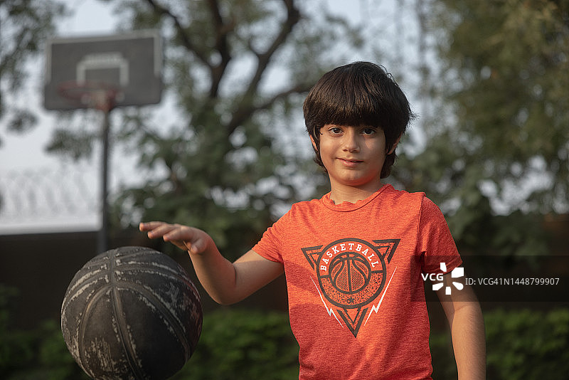 混血儿(印度-伊朗)8岁，打篮球，积极的生活方式。看着镜头微笑图片素材