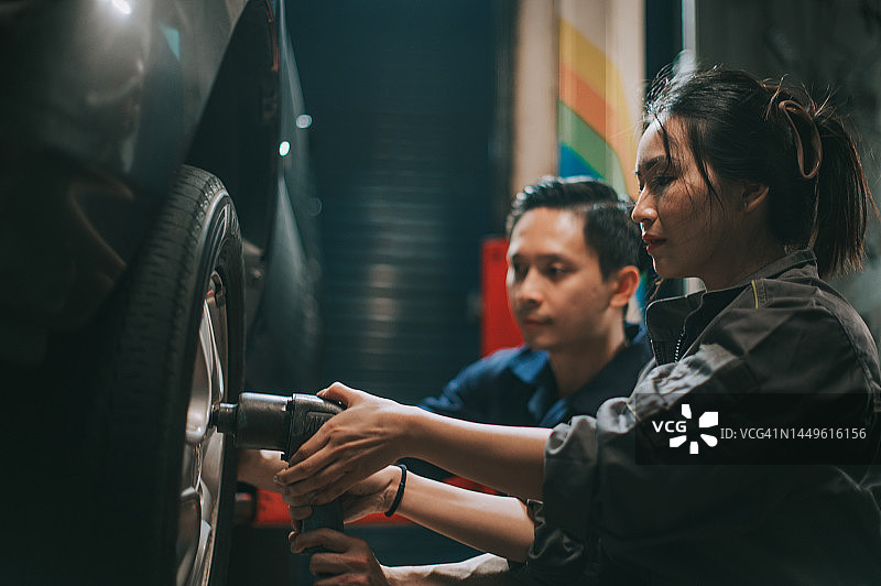 亚洲华人机械师在车间里教同事学徒换轮胎图片素材