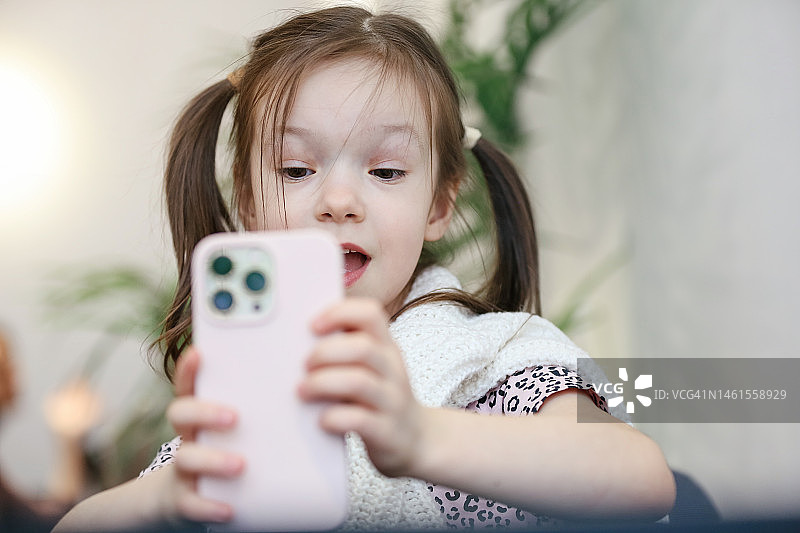 5-6岁的女孩用智能手机自拍，微笑，做鬼脸和直播图片素材