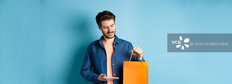 年轻的小伙子微笑着展示橙色购物袋，展示礼物图片素材