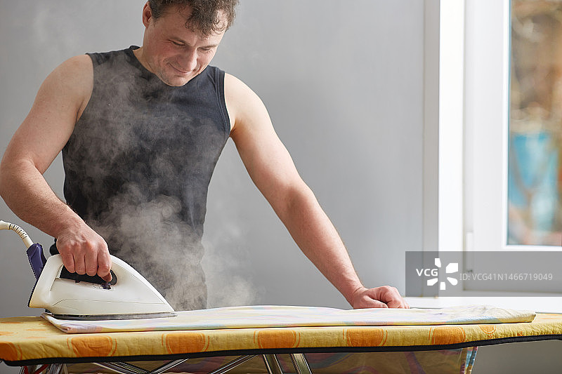 用蒸汽发生器熨衣服的男人蒸汽围绕照顾家庭的概念，帮助，俄罗斯图片素材