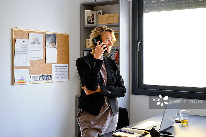 一个快乐的白人女性站在她的公寓里接工作电话图片素材