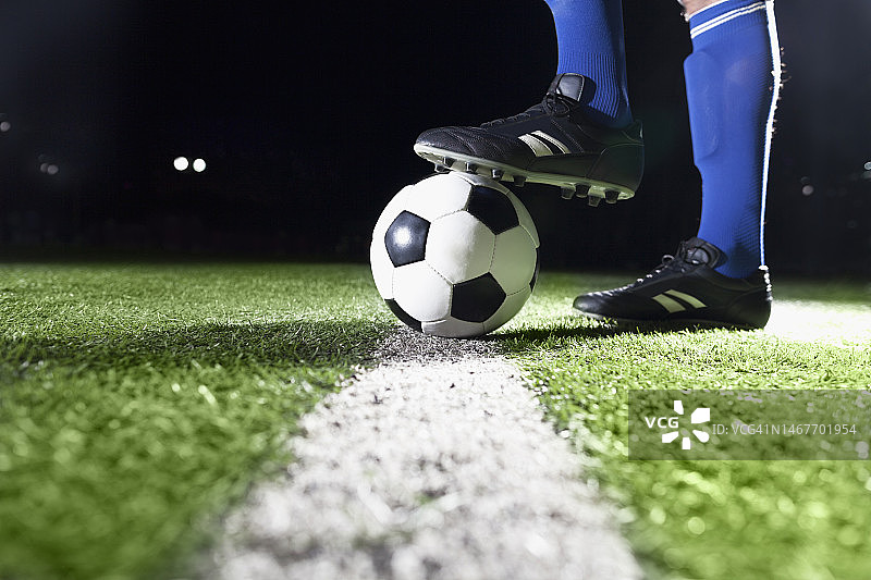 晚上，足球运动员的脚踩在足球场上图片素材