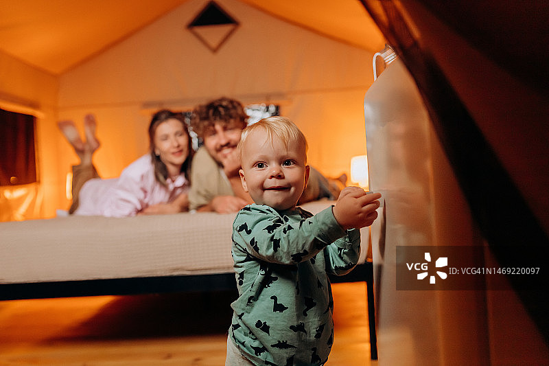 幸福的家庭，可爱的宝宝玩耍，夏天晚上躺在床上，一起度过舒适的豪华露营时光。户外休闲休闲的豪华露营帐篷图片素材