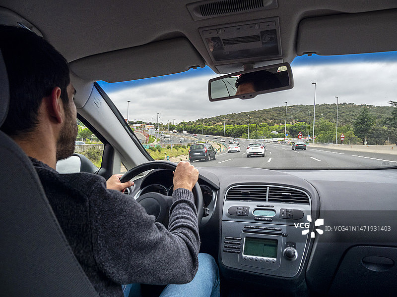 从汽车的角度来看，一个年轻人开着一辆车走在一条有很多车辆的双车道高速公路上图片素材