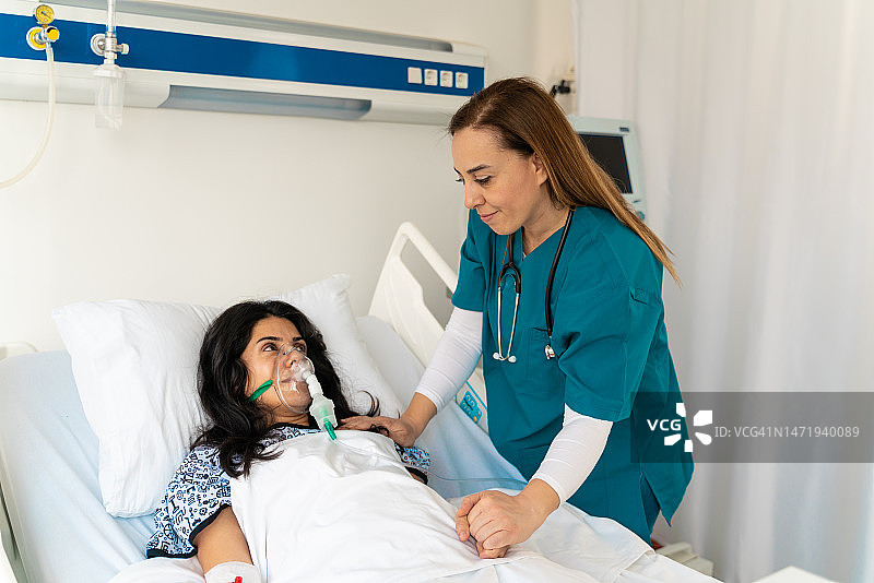 一名妇女戴着氧气面罩躺在病床上，与关怀的医生或护士手牵手图片素材
