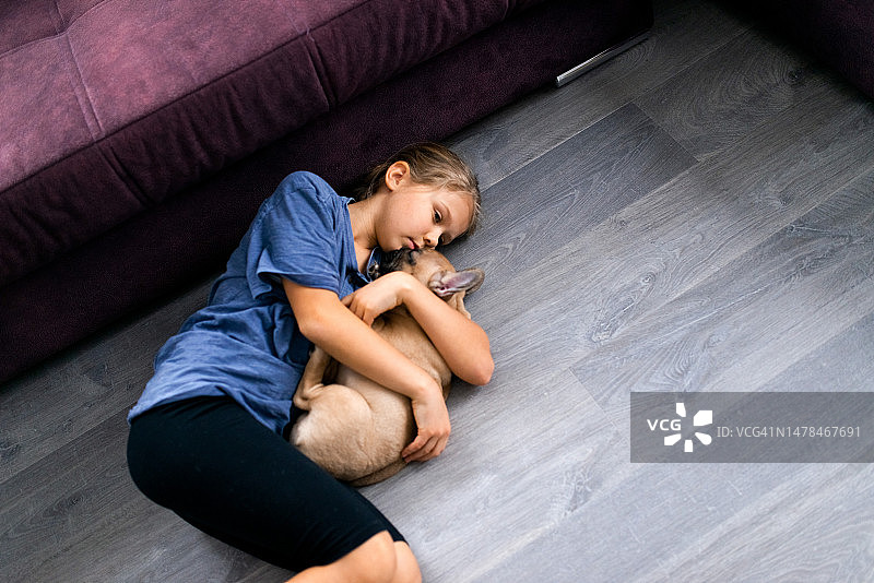 孩子抱着她的宠物，女孩躺在地板上与法国斗牛犬小狗图片素材
