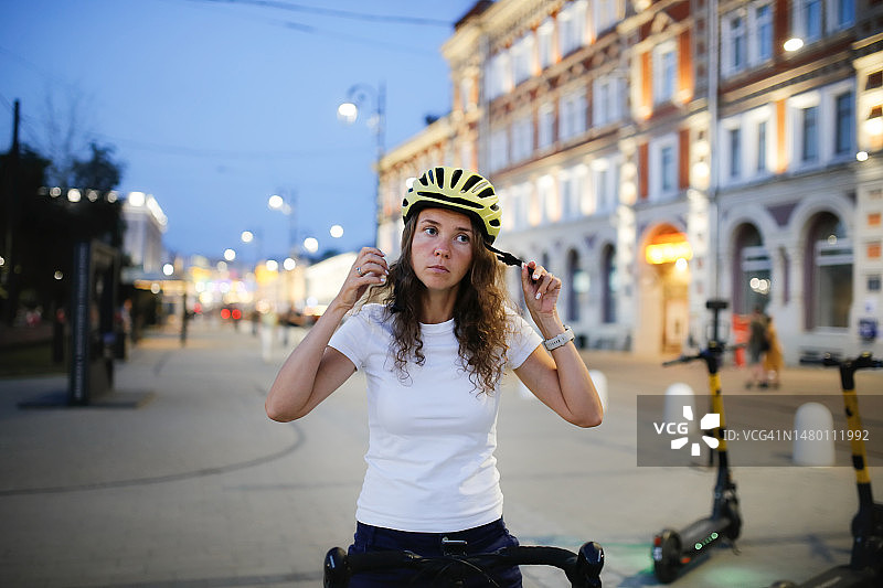 可爱的中年妇女在夜晚的城市街道上系上运动头盔。图片素材