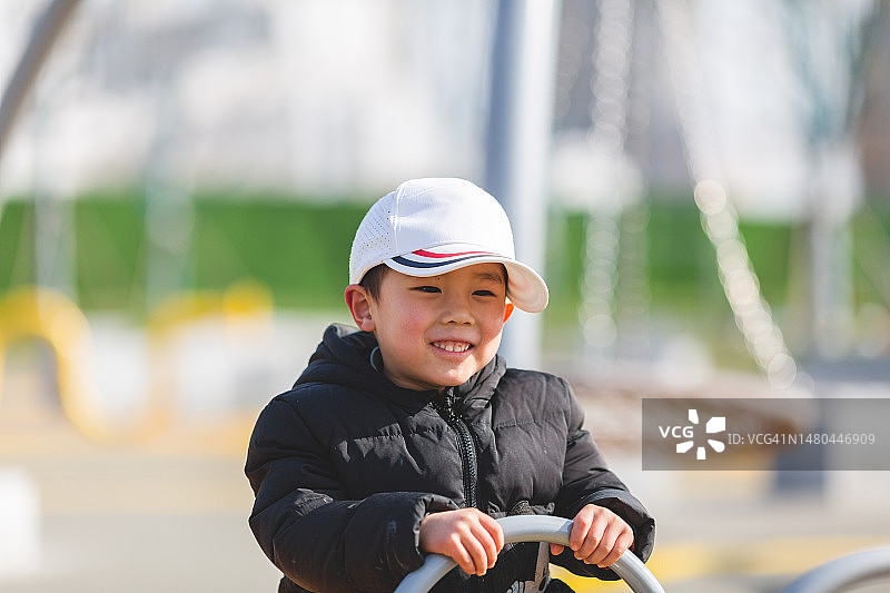 可爱的亚洲男孩在户外操场上玩跷跷板。图片素材