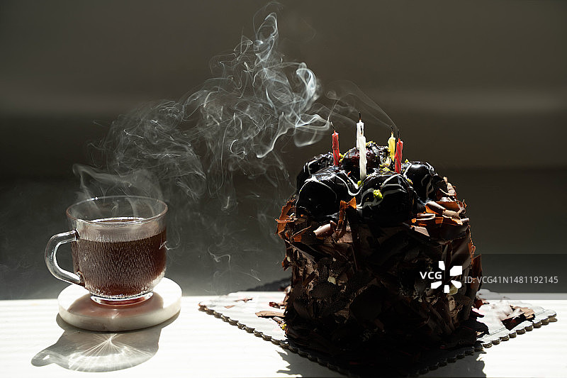 一个节日巧克力蛋糕，旁边有蜡烛和一杯热茶。图片素材