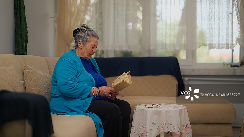 老年妇女坐在客厅的沙发上，享受读书图片素材