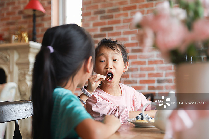亚洲双胞胎女孩在餐厅吃甜点。图片素材