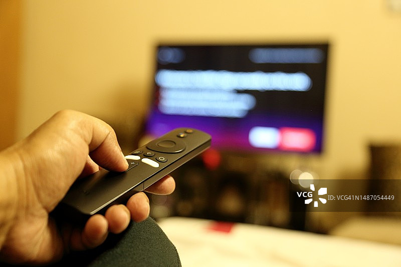 一个人的手将遥控器指向高清电视(HD TV)的特写。图片素材