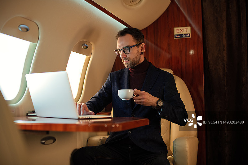 戴眼镜的优雅商人在私人飞机头等舱喝咖啡图片素材