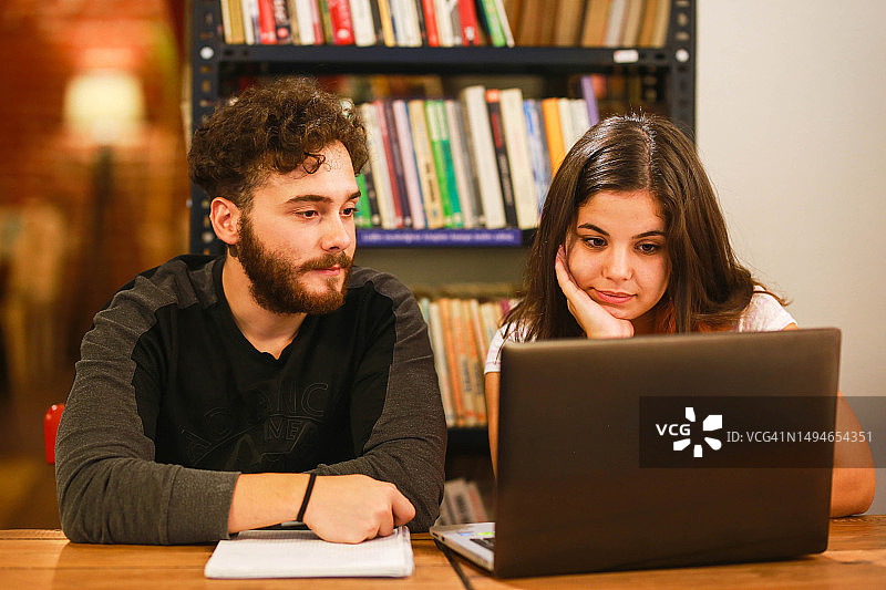 年轻的女人和年轻的男人一起在书咖啡馆用笔记本电脑学习。研究概念图片素材