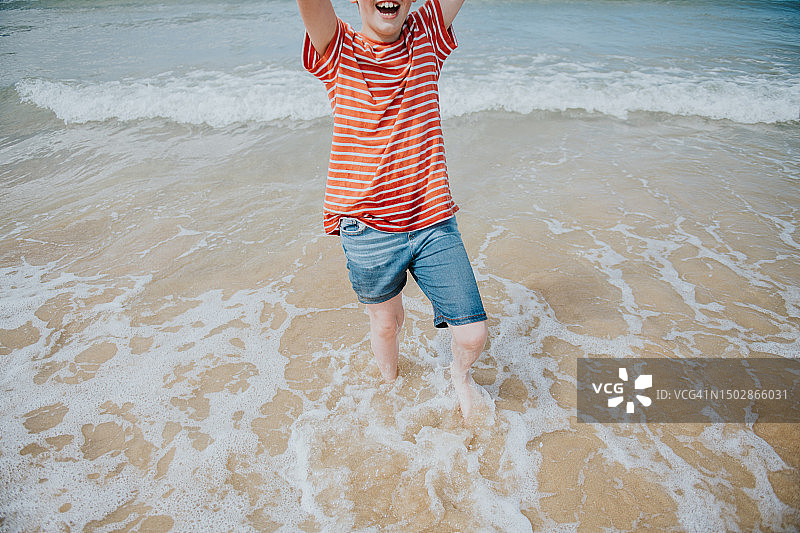 一个穿着红色条纹t恤的快乐的孩子举起双手，高兴地尖叫着图片素材