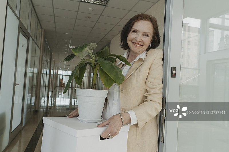 微笑的资深女商人在办公室走廊里拿着装有盆栽的盒子图片素材